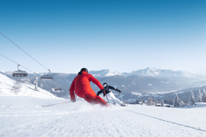 Two skiers carving on a wide, groomed slope with mountain view and sunshine